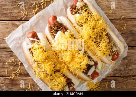 Rindfleisch Hot Dog in einem Brötchen mit Cincinnati Chili, gewürfelten Zwiebeln und einem Hügel mit geschreddertem Cheddar-Käse in der Nähe auf dem Papier auf dem Tisch bedeckt. Horizonta Stockfoto