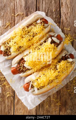 Leckere hausgemachte Cincinnati Chili Hot Dog mit Rinderwurst, Cheddar-Käse und Zwiebeln in der Nähe in das Papier. Vertikale Draufsicht von oben Stockfoto