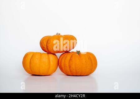 Drei kleine orangefarbene Kürbisse in einer Pyramide auf weiß isolierter Hintergrundansicht. Halloween und Thanksgiving Herbstkonzept Stockfoto