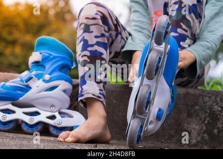 Nahaufnahme von asiatischen Kindern auf dem Boden beim Ausziehen oder Aufsetzen der Inline-Skates mit Rollerblade, die Schnürsenkel binden, während sie auf dem Fußweg im Park in da sitzen Stockfoto