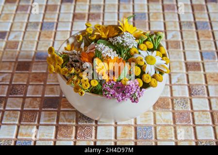 Auf der Arbeitsplatte befindet sich eine Keramikschale mit Heilkräutern und Blumen. Stockfoto