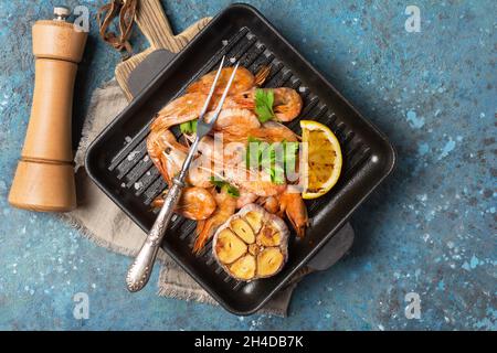 Draufsicht auf gegrillte Garnelen auf gusseiserner Pfanne oder Pfanne mit Gewürzen, gebratener Zitrone und Knoblauch auf blauem Beton-Hintergrund Stockfoto