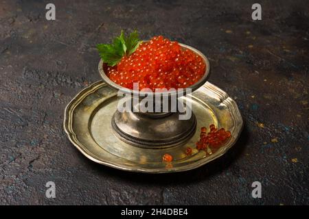 Vintage Silberschale mit appetitlich rotem Kaviar auf dunklem Beton-Hintergrund als Symbol des Luxuslebens Stockfoto