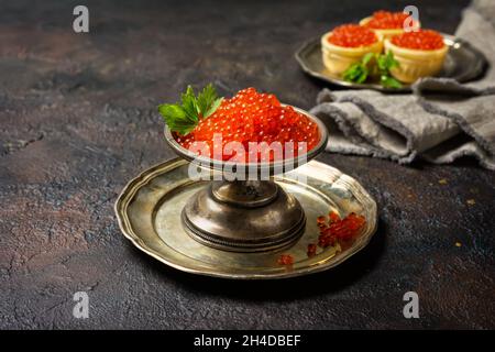 Vintage Silberschale mit appetitlich rotem Kaviar auf dunklem Beton-Hintergrund als Symbol des Luxuslebens Stockfoto