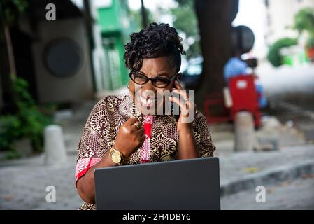 Schöne reife Geschäftsfrau in traditionellen Kleid sitzen im Freien auf dem Handy lachend reden. Stockfoto