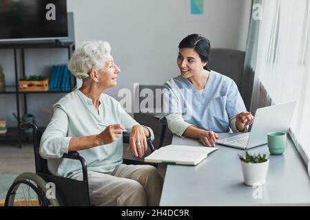 Porträt einer lächelnden Krankenschwester, die einer älteren Frau hilft, die zu Hause einen Laptop benutzt, um Platz zu kopieren Stockfoto