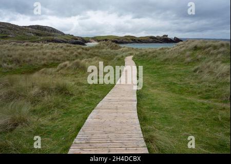 Clachtoll Beach in Assynt, schottische Highlands an einem bewölkten Tag mit dramatischem Himmel. Holzboardwalk, die durch Gras zum Strand führt. Stockfoto