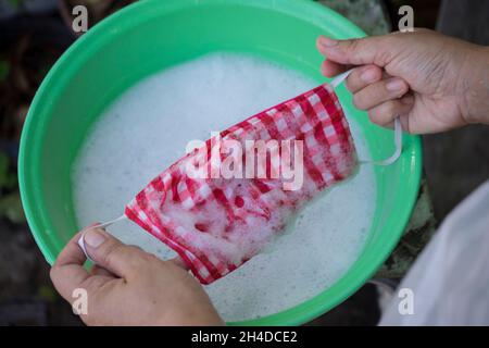 Frau Hand Waschen einer Maske mit in Wasser gelöstem Reinigungsmittel. Das Waschen der Masken desinfiziert und spart Geld, um wieder verwendet zu werden. Stockfoto