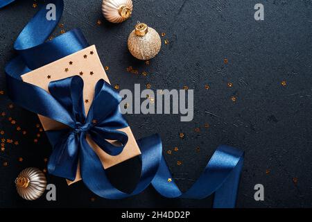 Geschenkschachtel oder Geschenk mit blauem Band, goldenem Konfetti und goldenen Kugeln auf schwarzem Hintergrund. Magische weihnachtsgrußkarte. Weihnachtsdekoration Stockfoto