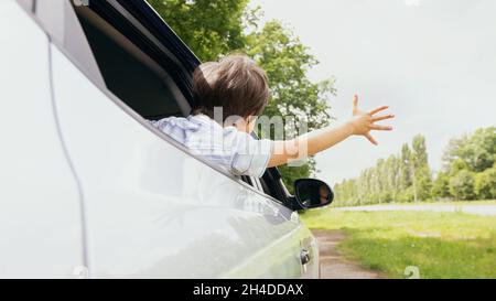 Kleiner Junge, der sich aus dem Autofenster lehnte und versuchte, Wind zu fangen Stockfoto