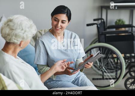 Lächelnde Krankenschwester mit digitalem Tablet, während sie ältere Frau im Altersheim vermessung, Kopierraum Stockfoto