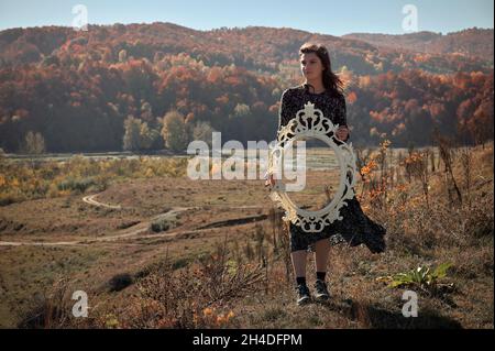Konzeptuelle junge Frau, die einen Spiegel in der Natur hält Stockfoto