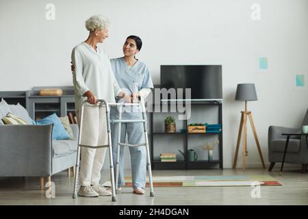 Porträt einer lächelnden Krankenschwester, die älteren Frauen mithilfe von Gehhilfen im Altersheim hilft, Kopierraum Stockfoto