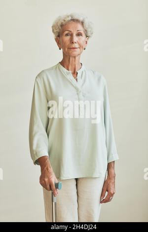 Vertikales Porträt einer eleganten älteren Frau, die vor neutralem Hintergrund auf die Kamera schaut Stockfoto