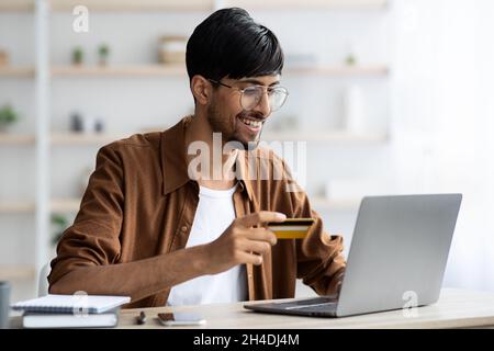 Glücklicher arabischer Mann, der im Internet einkaufen kann, während er im Büro sitzt Stockfoto