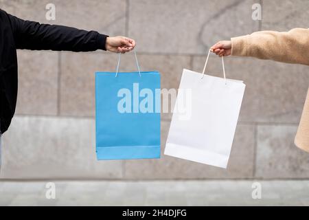 Beschnittene Ansicht von jungen Männern und Frauen, die Einkaufstaschen mit Mockup für Ihr Markenlogo in der Nähe einer Steinmauer halten Stockfoto