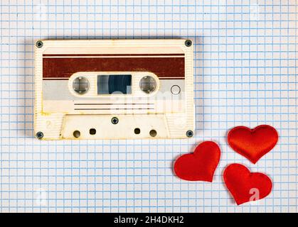 Alte Audiokassette mit roten Herzen auf dem quadratischen Papierhintergrund Nahaufnahme Stockfoto