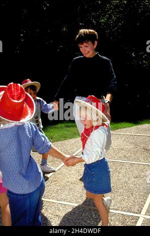Eine Mutter spielt auf einer Geburtstagsfeier mit Kindern, die tanzen und die Hände im Kreis halten. Stockfoto