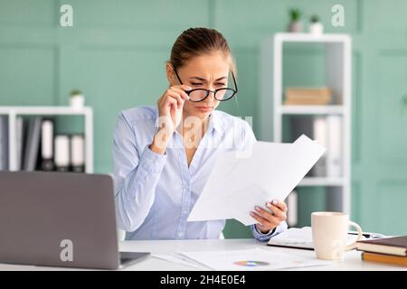 Weibliche Büroangestellte, die Papierarbeiten macht, Brillen trägt, Augenprobleme hat und Dokumente liest Stockfoto