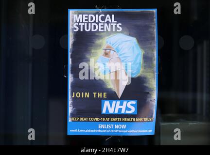 Ein Plakat, das zeigt, dass ein Mitarbeiter im Gesundheitswesen PSA (persönliche Schutzausrüstung) trägt und Medizinstudenten auffordert, sich dem NHS anzuschließen, um beim BAT covid-19 im Barts Health NHS Trust zu helfen, wird in einem Fenster vor dem Royal London Hospital in Whitechapel, East London, Das Vereinigte Königreich befindet sich weiterhin im Lockdown, um die Ausbreitung des Coronavirus einzudämmen. Bilddatum: Freitag, 24. April 2020. Stockfoto