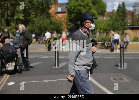 Ein älterer Mann mit Gesichtsmaske geht durch eine verkehrsreiche Straße am Broadway Market, Hackney, im Osten Londons, während Großbritannien weiterhin in der Sperre bleibt, um die Ausbreitung des Coronavirus einzudämmen. Bilddatum: Samstag, 2. Mai 2020. Stockfoto