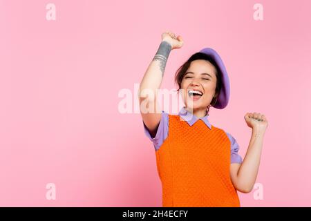 Aufgeregt tätowierte Frau zeigt jubeln Geste und Schreien isoliert auf rosa Stockfoto