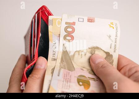 Die Hand des Mannes zieht die Griwna-Banknoten aus der roten Brieftasche, um die Dienstleistungen, die Kredite zu bezahlen Stockfoto