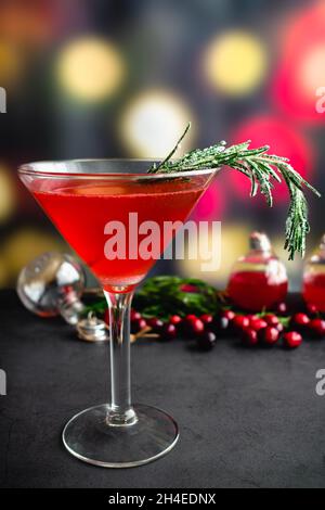 Holiday Gin und Tonic garniert mit Frosted Rosmarin: Ein Cranberry- und Gin-Cocktail, der in einem martini-Glas serviert wird und mit einem gezuckerten Rosmarin-Zweig garniert ist Stockfoto