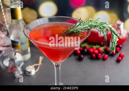 Holiday Gin und Tonic garniert mit Frosted Rosmarin: Ein Cranberry- und Gin-Cocktail, der in einem martini-Glas serviert wird und mit einem gezuckerten Rosmarin-Zweig garniert ist Stockfoto