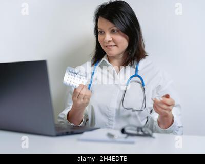 ärztin in weißer medizinischer Uniform mit Stethoskop mit Computer-Laptop, die Videokonferenz mit dem Patienten am Schreibtisch in der Klinik oder der Klinik spricht Stockfoto