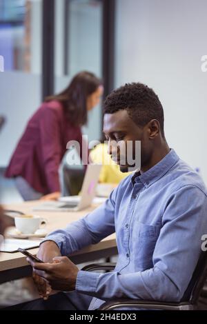 afroamerikanischer behinderter Geschäftsmann mit Smartphone und im Rollstuhl sitzend in einem modernen Büro Stockfoto