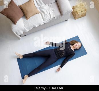 Junge schlanke, schöne Frau, die sich in Shavasana-Yoga-Pose auf der Matte legt Stockfoto