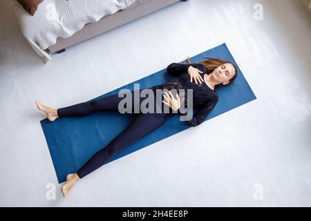 Junge schlanke, schöne Frau, die sich in Shavasana-Yoga-Pose auf der Matte legt Stockfoto