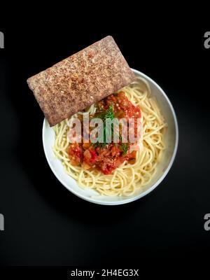 Pasta mit Tomatensauce in runder Schüssel mit Cracker mit dunklem Hintergrund Draufsicht Stockfoto