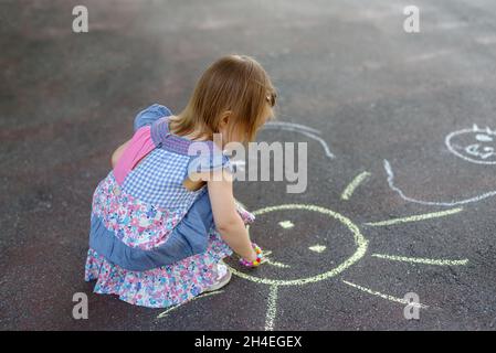 Aufnahme eines kleinen Mädchens, das in farbenprächtiger Kreide auf dem Bürgersteig gezeichnet hat Stockfoto