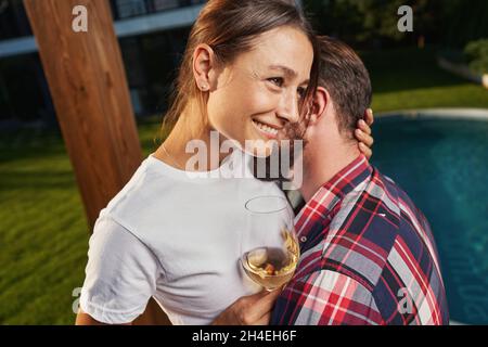Charmante Frau hält Glas mit Getränk und umarmt Mann in th im Freien Stockfoto