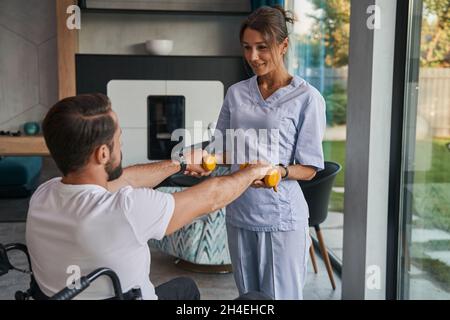 Charmante Frau Physiotherapeutin hilft mit Rehabilitationsübungen im Zimmer drinnen Stockfoto