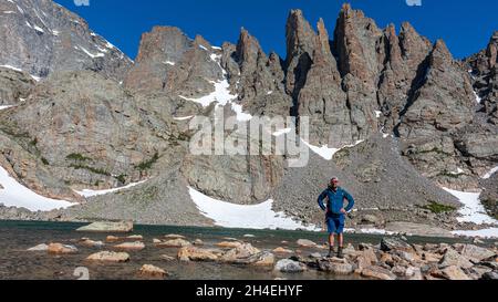 Wanderer, der auf einem Felsen am Sky Pond steht, mit dem Hai-Zahn im Hintergrund Stockfoto