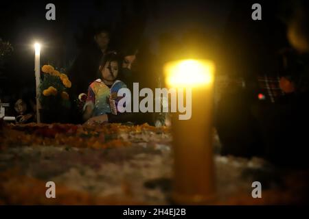 Eine Person hält einen Abend auf dem Friedhof von San Pedro Tláhuac ab, um die Ankunft ihrer verstorbenen Angehörigen zu erwarten, Verwandte schmücken Blumen, Bringen Sie ihnen Essen und singen Sie ihnen an den Gräbern als mexikanische Traditionen des Tages der Toten, um ihnen eine gute Rückkehr auf dem Weg nach Mictlan zu wünschen. Am 1. November 2021 in Mexiko-Stadt, Mexiko. (Foto von Fernanda Rojas/ Eyepix Group) Stockfoto