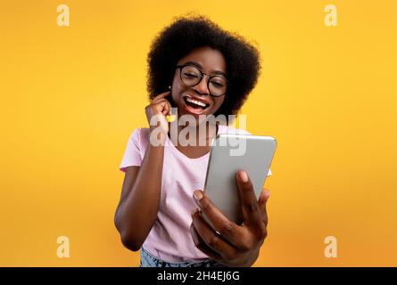 Glückliche afroamerikanische Dame mit Smartphone und macht Videoanruf, lächelnd auf Handykamera über gelbem Hintergrund Stockfoto