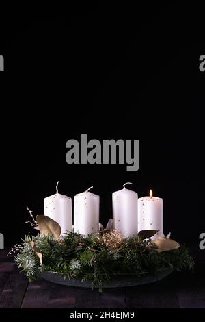 Erster Advent - Adventskranz aus Tanne und immergrünen Ästen mit weißen brennenden Kerzen auf dunklem Holztisch. Tradition in der Zeit vor Weihnachten. Stockfoto