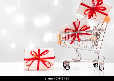 Weihnachtseinkäufe. Mini-Wagen mit Geschenken auf weißem Hintergrund mit Lichtern. Stockfoto