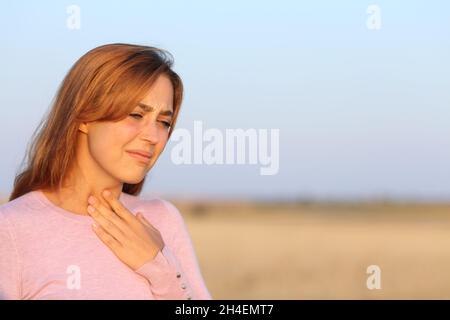 Gestresste Frau mit Halsschmerzen auf einem Feld Stockfoto