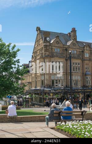 Harrogate People, Blick im Sommer auf Menschen, die sich in den Cenotaph Gardens entspannen und auf Bettys Cafe Tea Rooms im Zentrum von Harrogate, England, Großbritannien, schauen Stockfoto