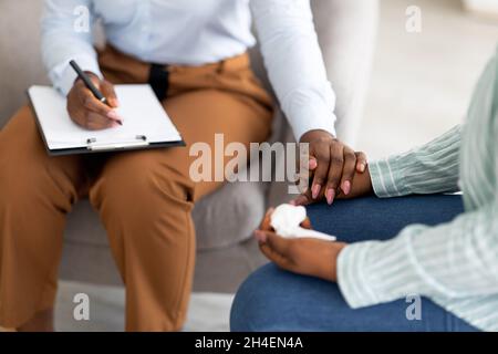 Psychotherapeutin, die junge Frau unterstützt, ihre Hand in der Klinik hält, beschnittene Ansicht Stockfoto