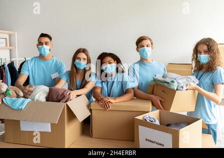 Konzept der Obdachlosenbetreuung. Junge Freiwillige in medizinischen Gesichtsmasken sortieren Kleiderspenden, arbeiten im Charity Center Stockfoto