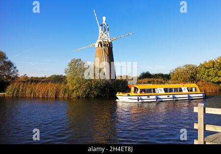 Ein Kreuzer, der an der Turf Fen Drainage Mill auf dem Fluss Ant auf den Norfolk Broads von How Hill, Ludham, Norfolk, England, Großbritannien vorbeifährt. Stockfoto