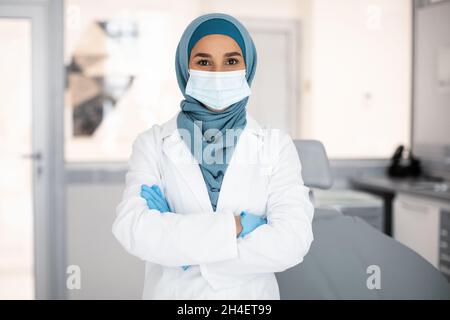 Selbstbewusste Muslim Stomatologin Trägt Hijab Und Posiert In Uniform Im Clinic Interior Stockfoto