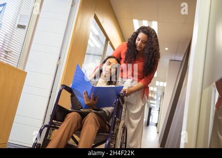 Biracial Geschäftsfrau im Rollstuhl im Gespräch mit biracial Geschäftsfrau in modernen Büro Stockfoto
