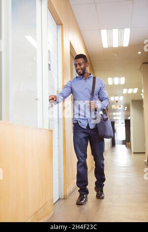 Lächelnder afroamerikanischer Geschäftsmann, der in einem modernen Büro die Tür auf dem Flur öffnet Stockfoto